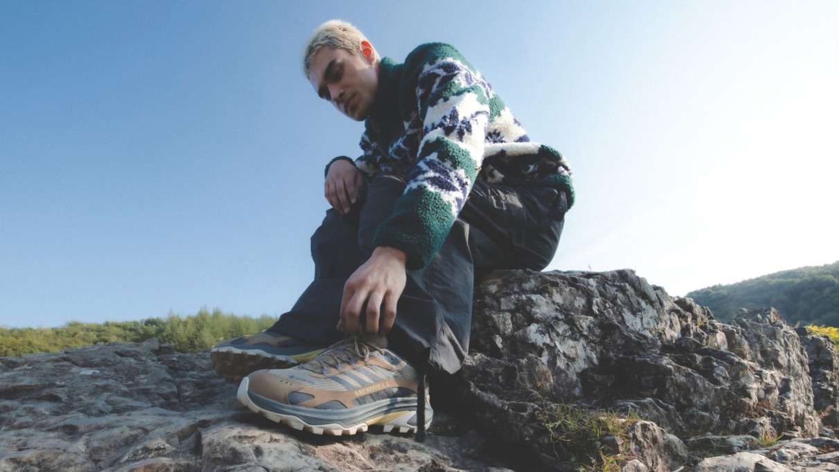 Man strikt zijn wandelschoenen van Merrell op een rotsachtig pad in de Ardennen