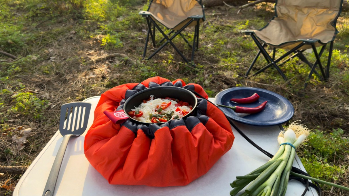 Pan met maaltijd in een feloranje EcoStoof Adventure op een kampeertafel in het bos