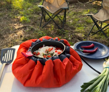 Pan met maaltijd in een feloranje EcoStoof Adventure op een kampeertafel in het bos
