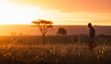 Masai-krijger loopt door hoog gras tijdens zonsondergang in de Masai Mara in Kenia