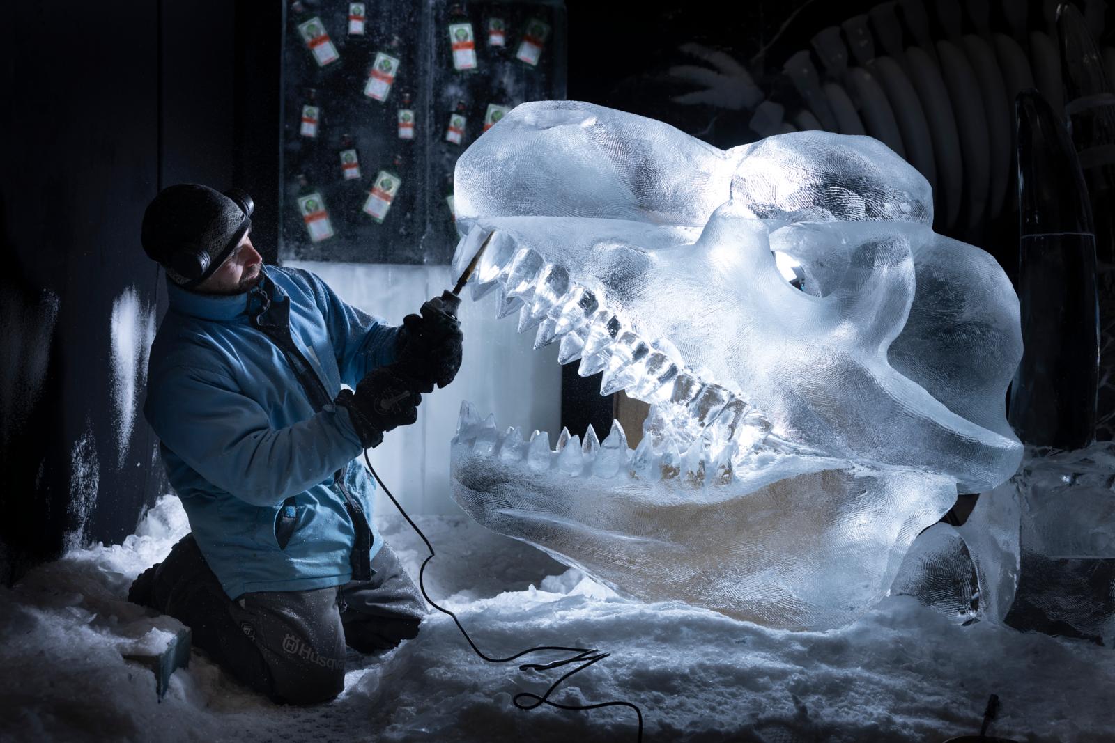 IJskunstenaar snijdt een grote dinoschedel uit helder ijs met een motorzaag in een ijzige werkruimte.