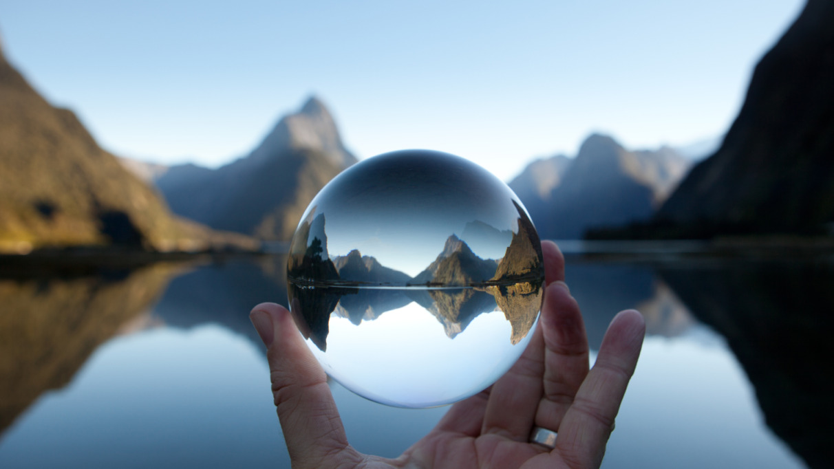 Man houdt kristallen bal vast met Mitre-piek reflecterend in Milford Sound, Nieuw-Zeeland