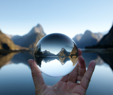 Man houdt kristallen bal vast met Mitre-piek reflecterend in Milford Sound, Nieuw-Zeeland