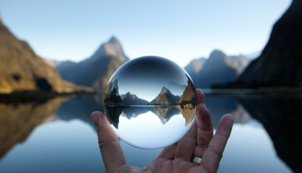 Man houdt kristallen bal vast met Mitre-piek reflecterend in Milford Sound, Nieuw-Zeeland