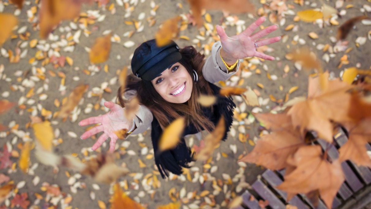 Vrouw gooit vrolijk herfstbladeren in de lucht