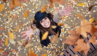 Vrouw gooit vrolijk herfstbladeren in de lucht