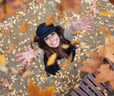 Vrouw gooit vrolijk herfstbladeren in de lucht