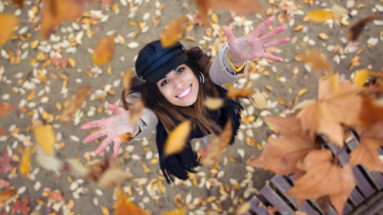 Vrouw gooit vrolijk herfstbladeren in de lucht