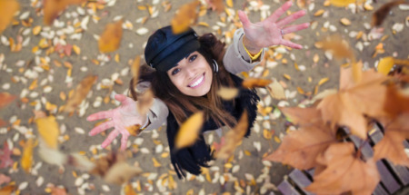 Vrouw gooit vrolijk herfstbladeren in de lucht