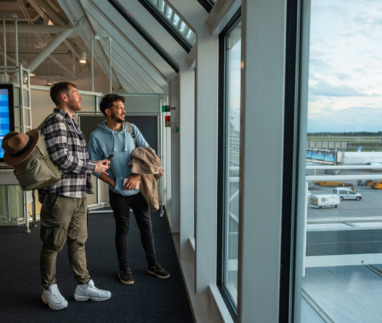 Twee vrienden kijken door het raam uit over Dusseldorf Airport