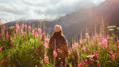Vrouw staat in zonlicht tussen lupines in de bergen