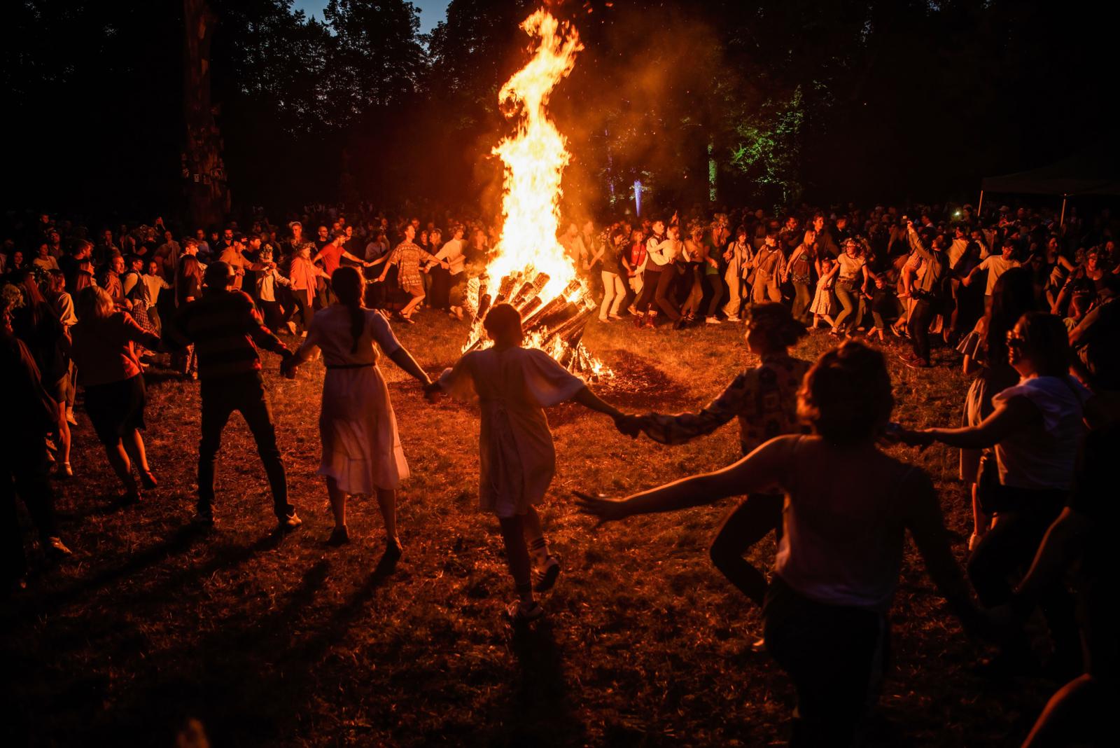 Mensen dansen hand in hand rond een groot vreugdevuur tijdens een zomers midzomerfeest in Litouwen.