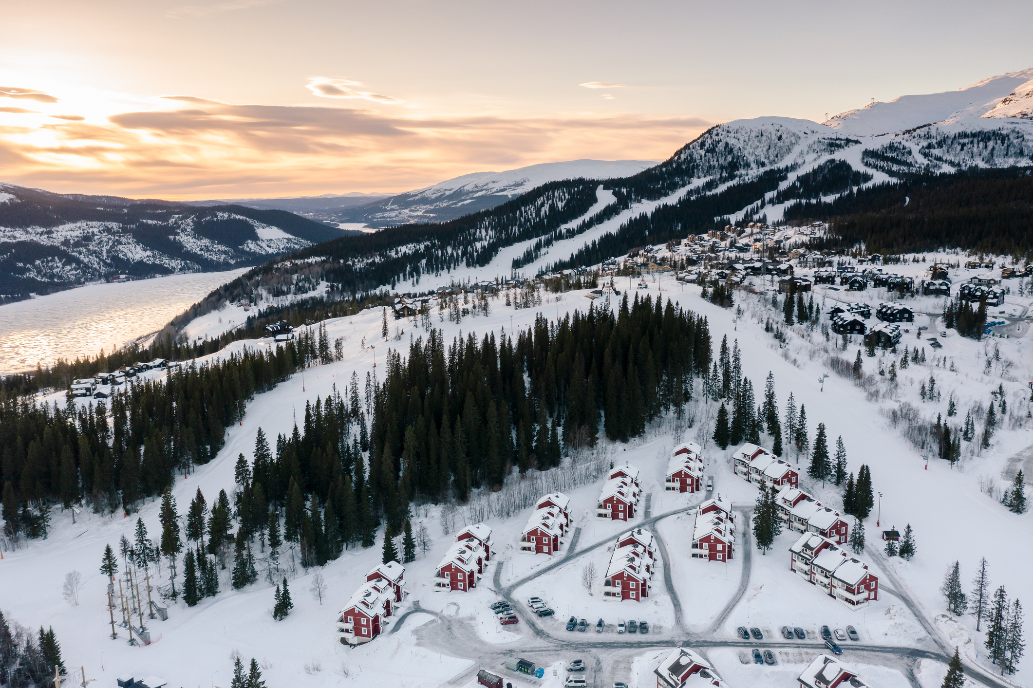 Sneeuwbedekt vakantiepark met rode houten huizen in de Zweedse bergen bij zonsondergang.