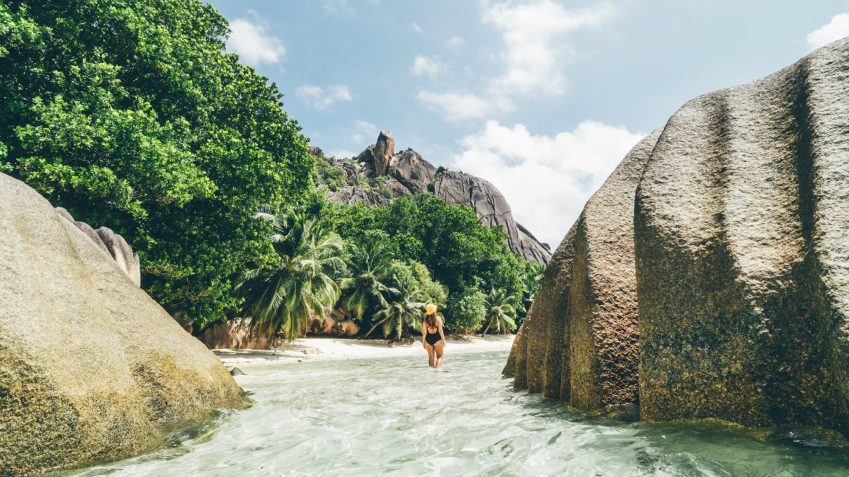 Jonge vrouw wandelt doo het ondiepe water bij het strand op de Seychellen