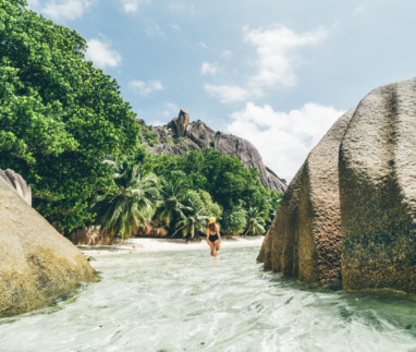 Jonge vrouw wandelt doo het ondiepe water bij het strand op de Seychellen