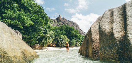 Jonge vrouw wandelt doo het ondiepe water bij het strand op de Seychellen