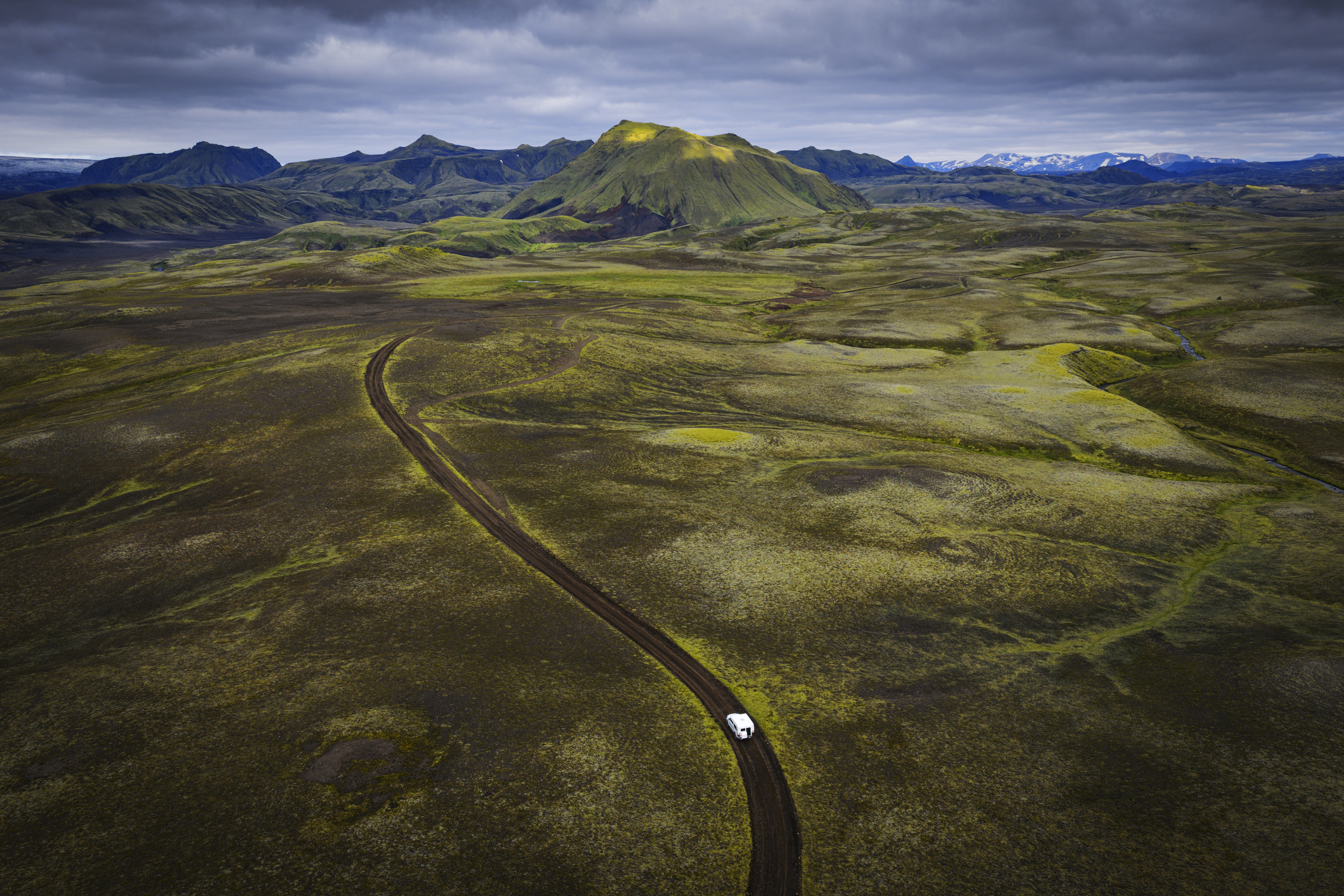 Auto op een onverharde weg door groen en vulkanisch landschap in het IJslandse binnenland.