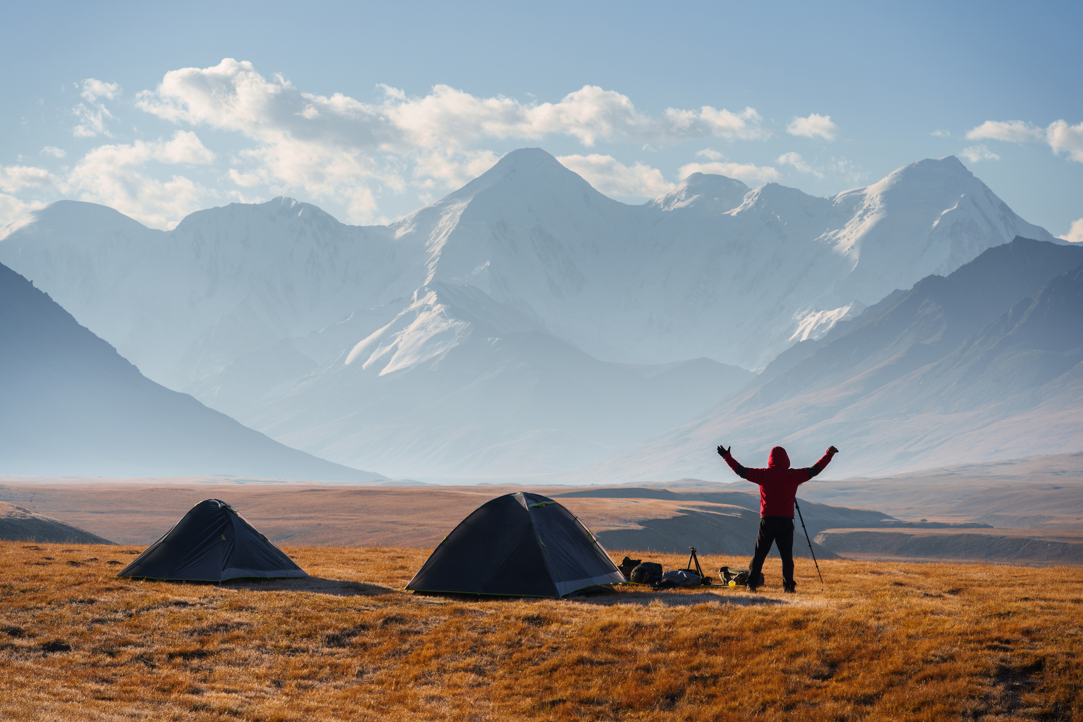 Kampeerders bij tenten in een uitgestrekte bergvallei in Kirgizië, met besneeuwde pieken op de achtergrond.