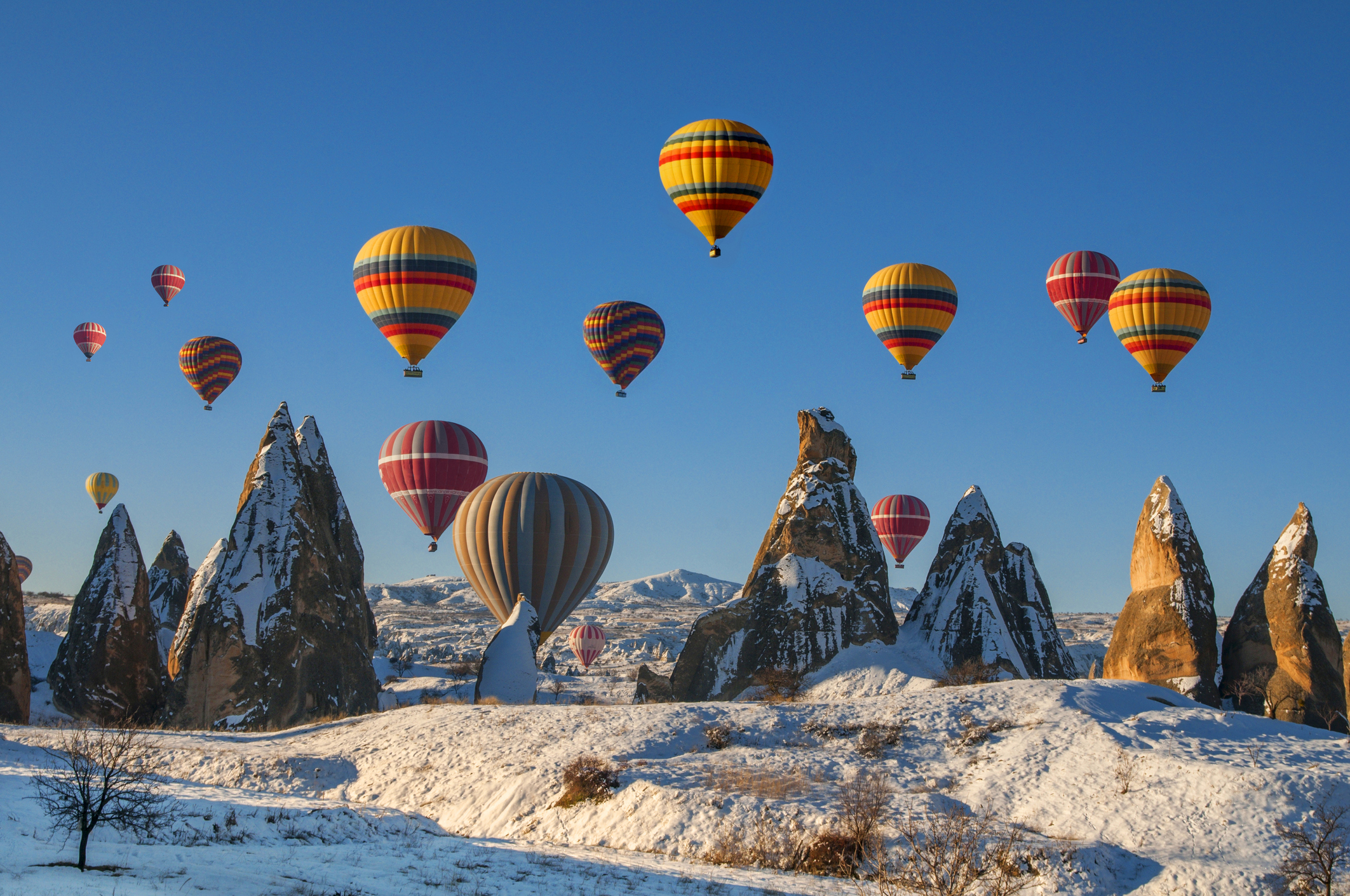 Gekleurde luchtballonnen zweven boven besneeuwde rotsformaties in Cappadocië, Turkije.