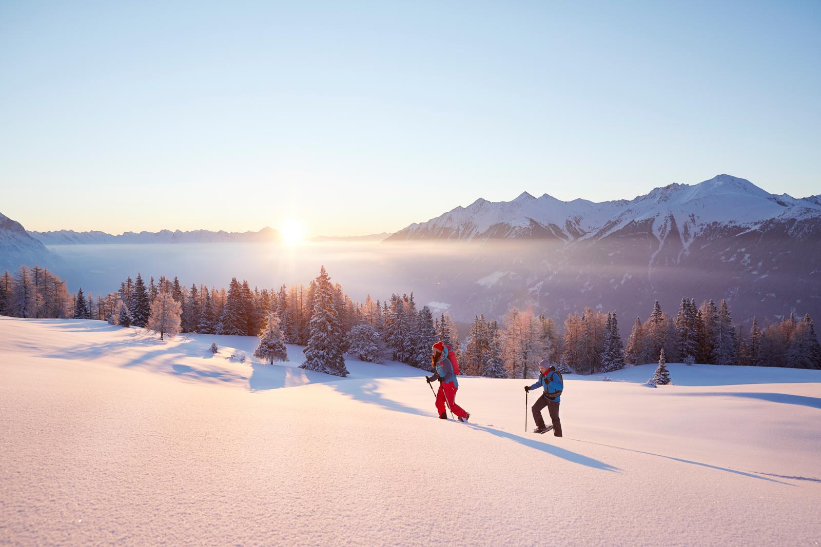 Twee sneeuwschoenwandelaars trekken door een besneeuwd berglandschap in Tirol bij zonsopkomst.