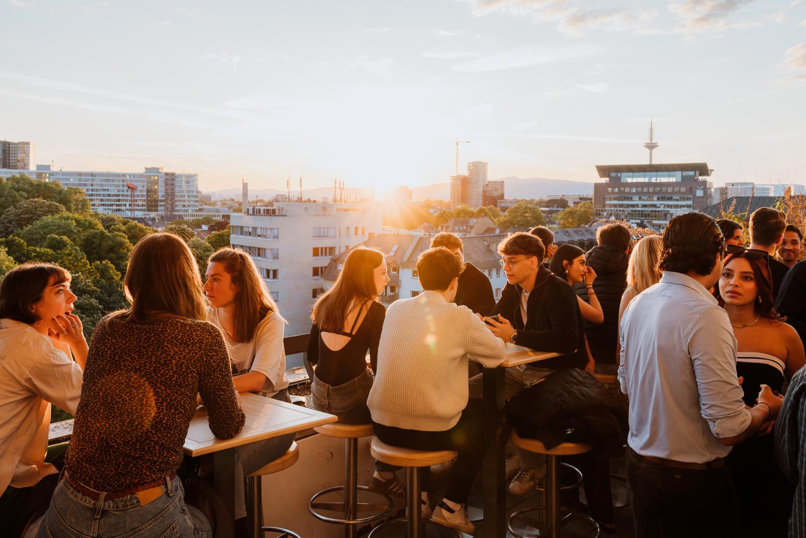 Bezoekers genieten van drankjes op een rooftop bar in Frankfurt bij zonsondergang.