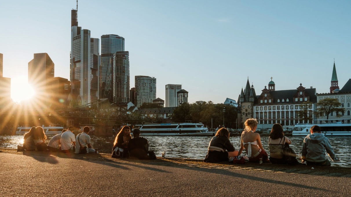 Jongeren aan de oever van de Main met skyline van Frankfurt bij zonsondergang.