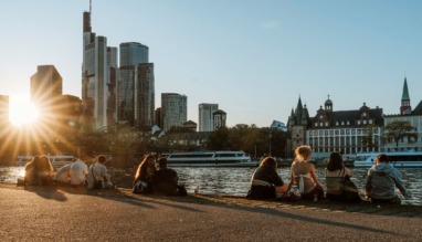 Jongeren aan de oever van de Main met skyline van Frankfurt bij zonsondergang.