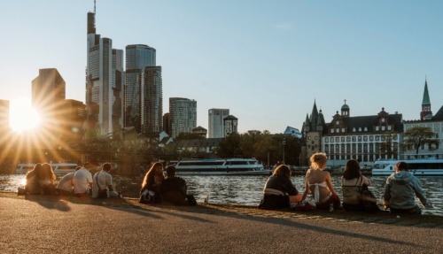 Jongeren aan de oever van de Main met skyline van Frankfurt bij zonsondergang.
