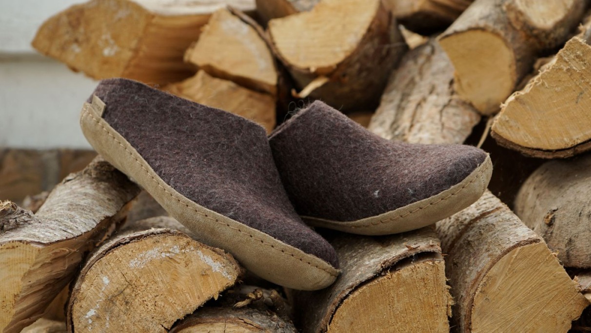 Bruine Glerups slippers van wol met leren zool, geplaatst op een stapel haardhout