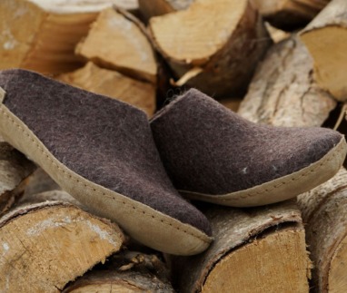 Bruine Glerups slippers van wol met leren zool, geplaatst op een stapel haardhout