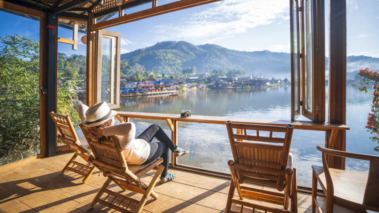 Vrouw relaxt in tuinstoel in een serre met uitzicht op een meer in Thailand