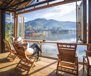 Vrouw relaxt in tuinstoel in een serre met uitzicht op een meer in Thailand
