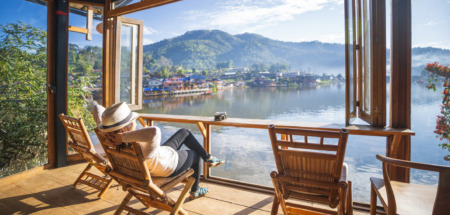 Vrouw relaxt in tuinstoel in een serre met uitzicht op een meer in Thailand