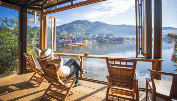 Vrouw relaxt in tuinstoel in een serre met uitzicht op een meer in Thailand