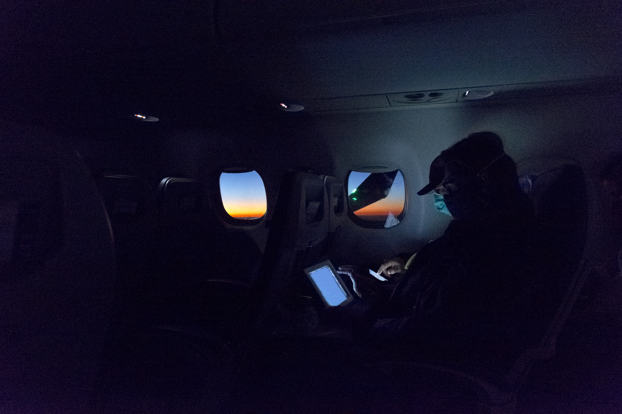 Passagier zit op een tablet in een gedimde cabine van het vliegtuig terwijl de zon opkomt