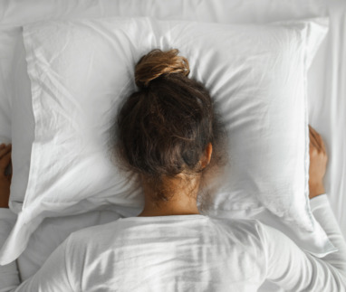 Vrouw ligt met hoofd in kussen in poging in slaap te vallen