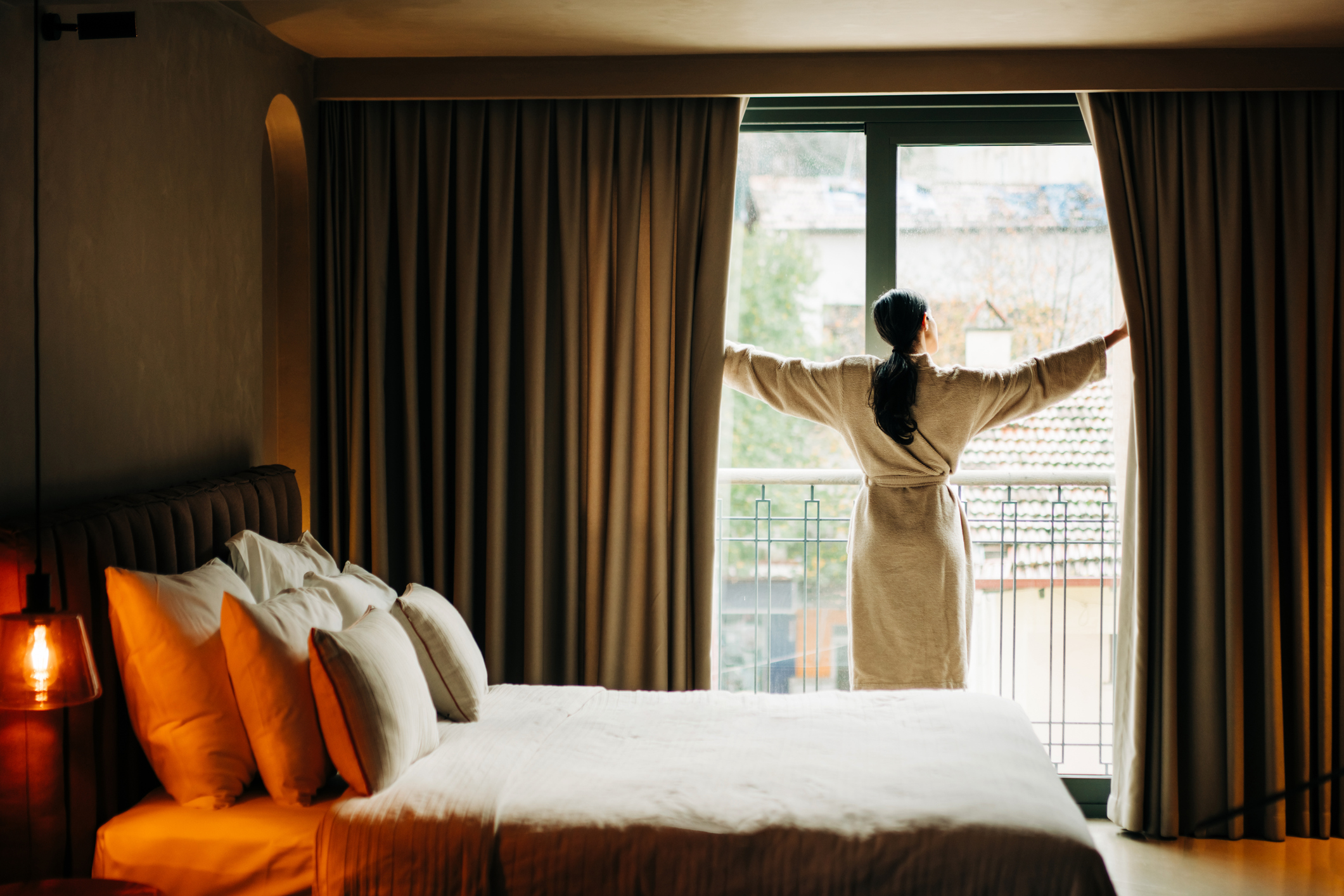 Vrouw opent de gordijnen van haar hotelkamer om het daglicht binnen te laten