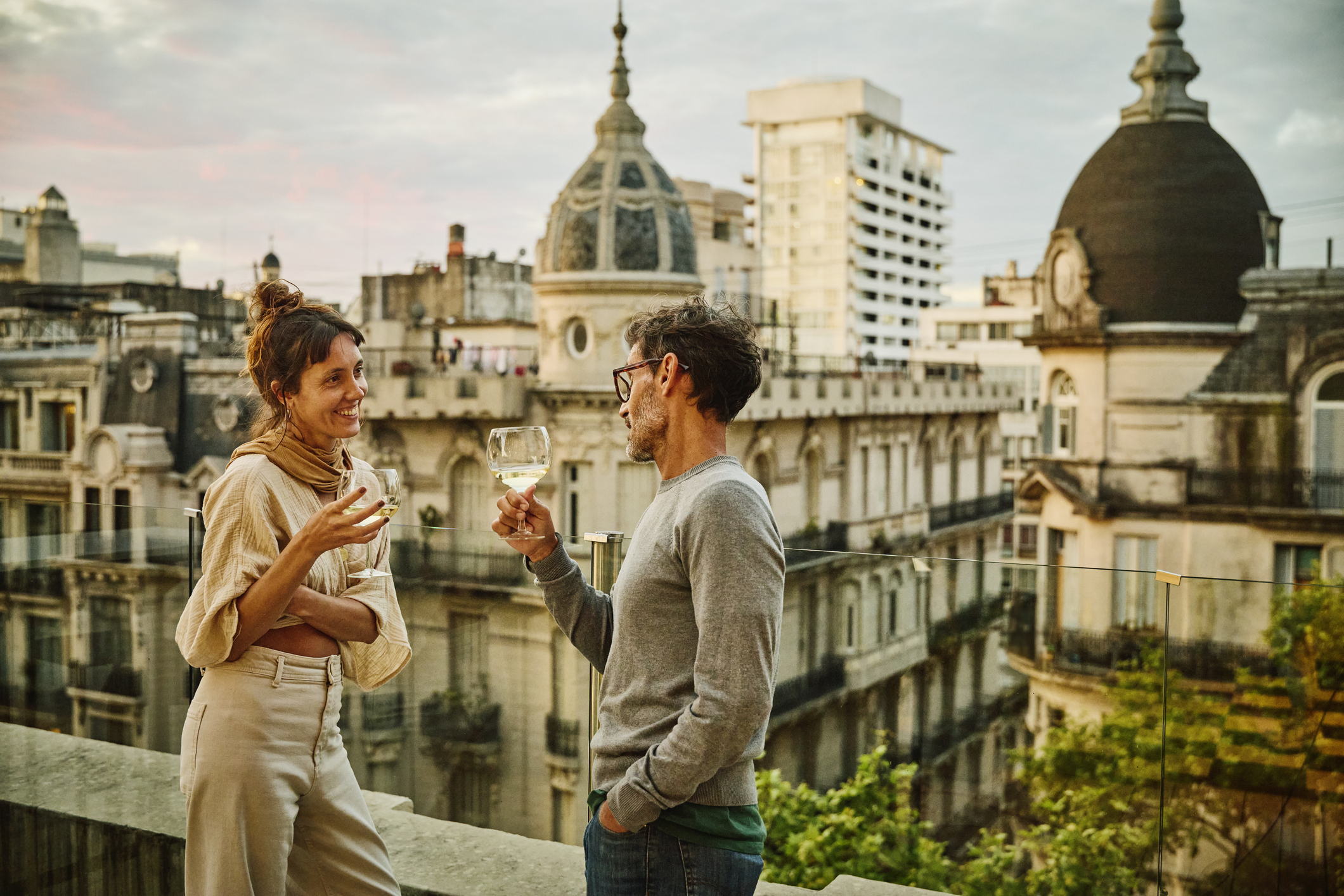 Stelletje staat op een rooftop in de stad met en glas wijn een geanimeerd gesprek te voeren