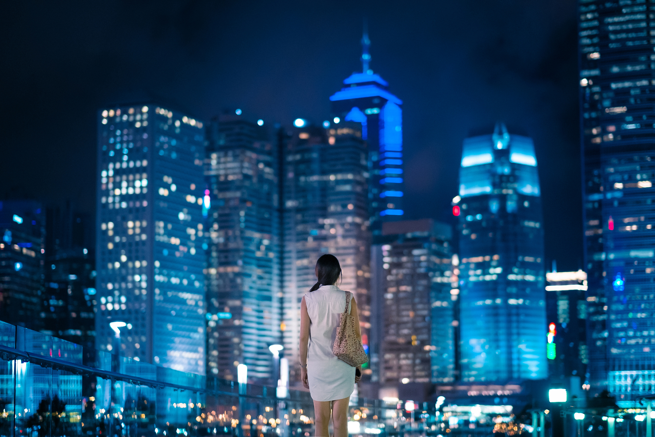 Vrouw kijkt uit over de skyline van Hongkong, China met enorme wolkenkrabbers die de avondhemel verlichten