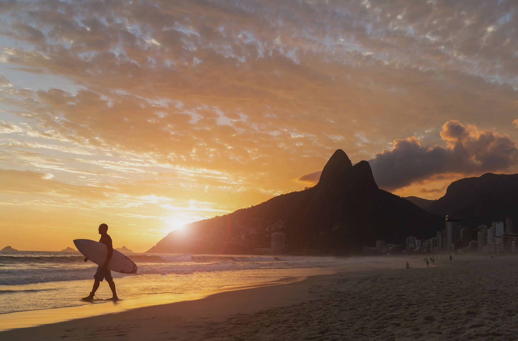 Surfer loopt met plank onder zn arm tijdens zonsondergang richting zee op Copacabana beach in Rio de Janeiro, Brazilië