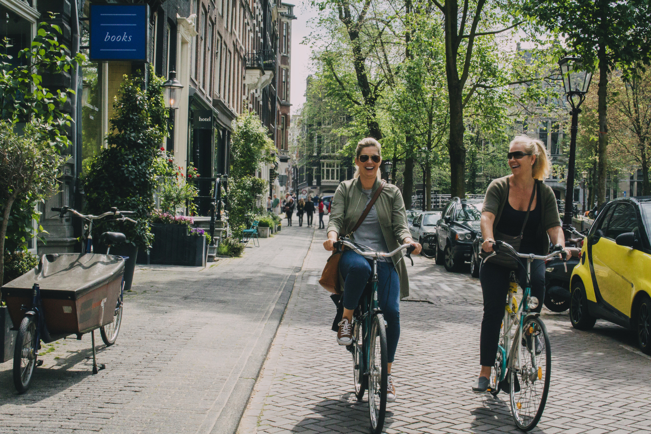 Twee Nederlandse vrouwen met zonnebrillen open fietsen over de grachten van Amsterdam in de zomer