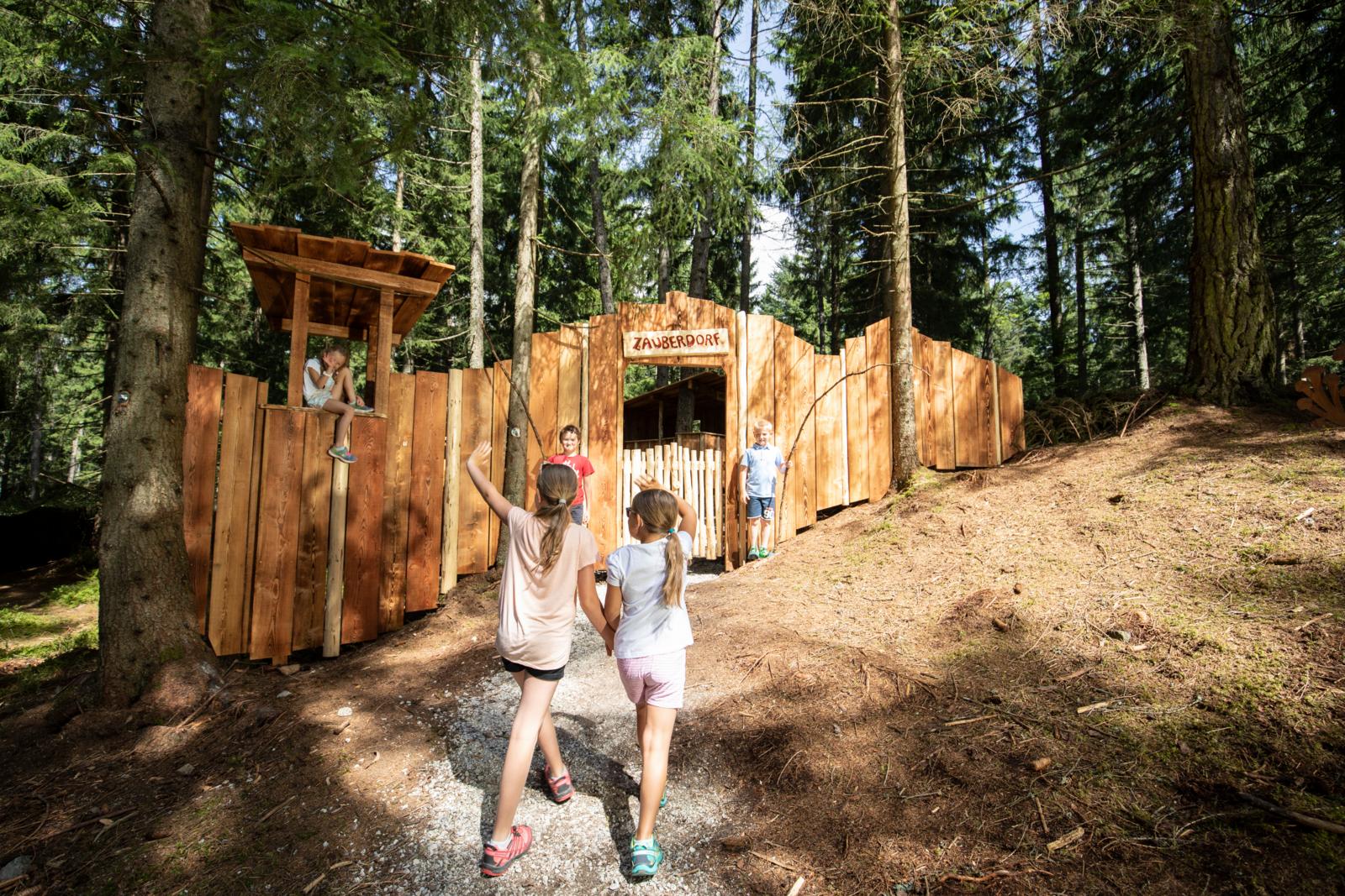 Kinderen spelen bij een houten speelplek in een bos in de Alpen.