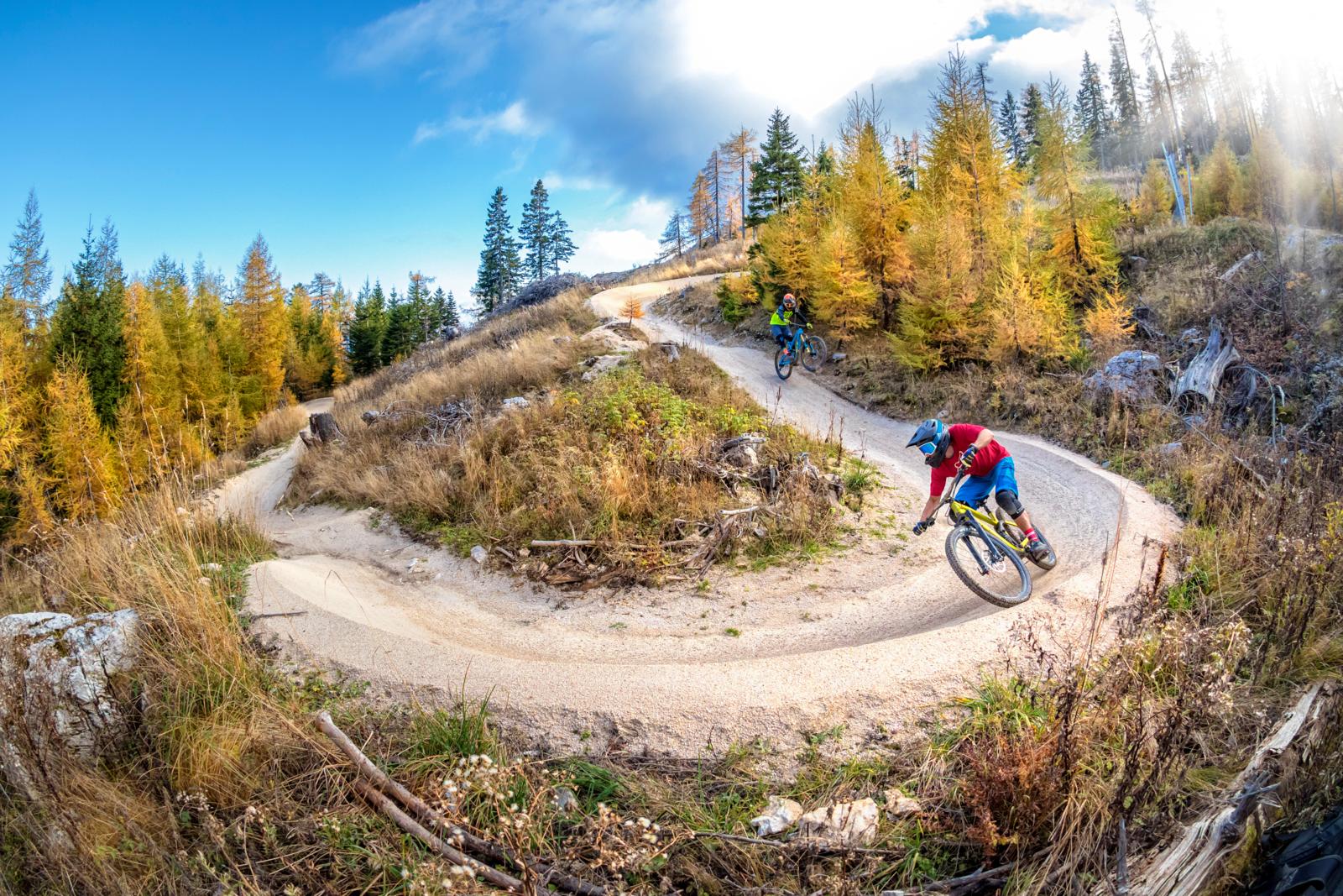 Mountainbikers op een bochtige flowtrail door herfstbos in de Oostenrijkse Alpen.