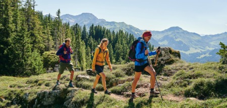 Wandelaars met rugzakken op een bergpad in de Bregenzerwald, omringd door bossen en bergen.