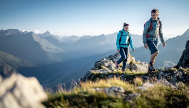 Twee wandelaars lopen over een bergkam met uitzicht op de Alpen.