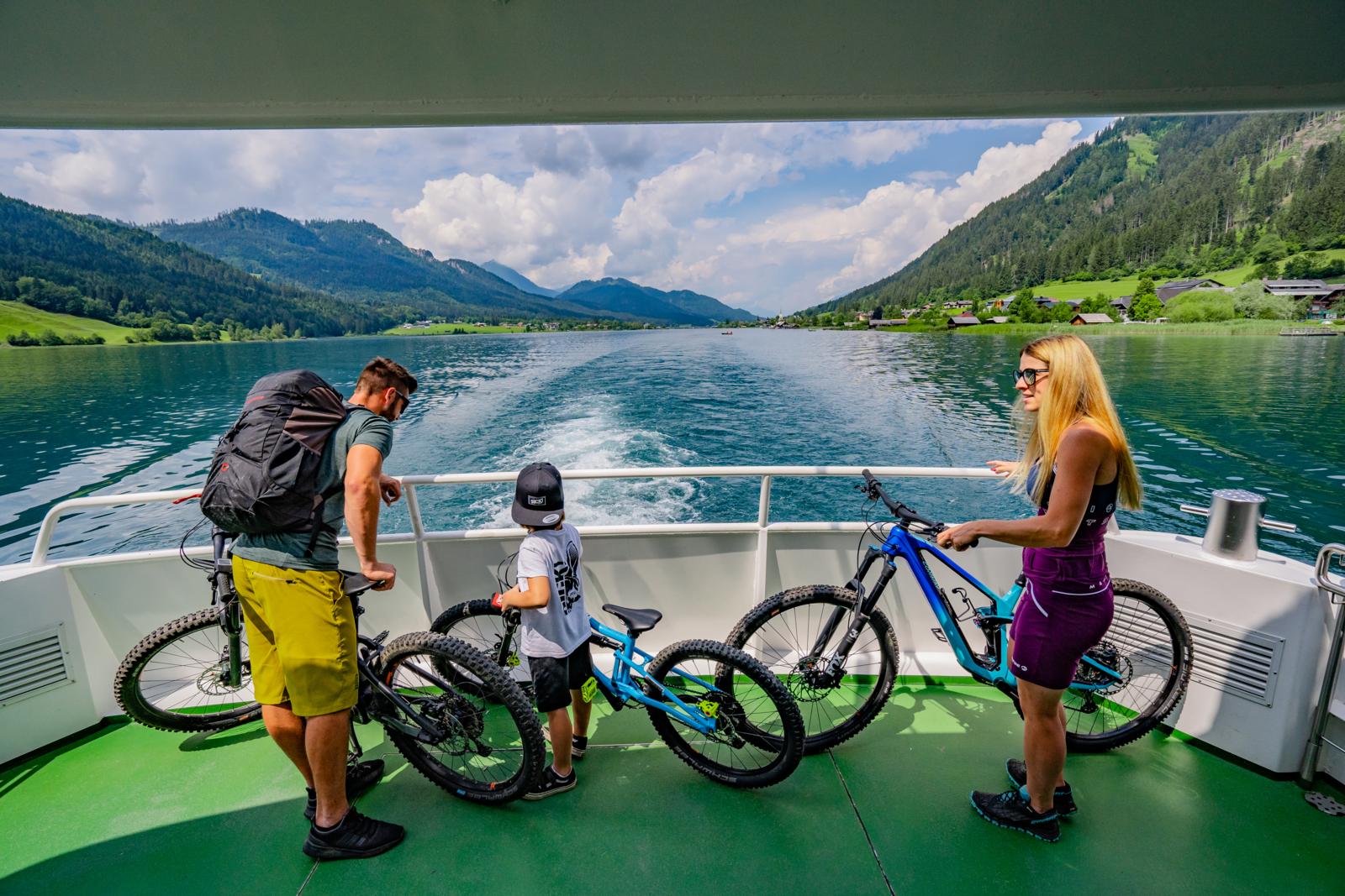 Gezin met fietsen op een veerpont op de Weissensee, omringd door bergen in Karinthië, Oostenrijk.