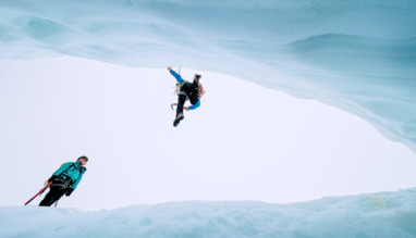 Twee hikers springen over gat in glacier
