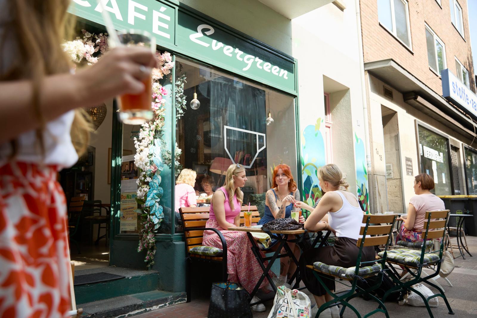 Terras van Café Evergreen in Duisburg met jonge mensen die buiten zitten en drankjes drinken.
