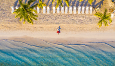Vrouw in rode rok ligt op idyllisch tropisch strand onder palmbomen