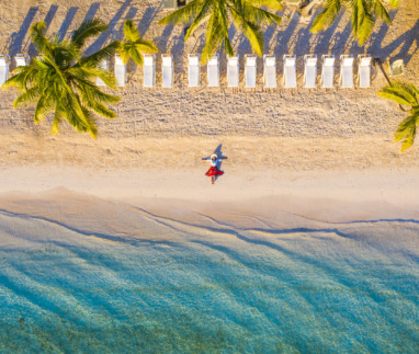 Vrouw in rode rok ligt op idyllisch tropisch strand onder palmbomen